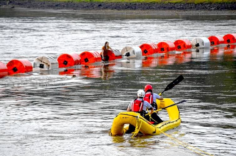 A Worthington BoatBuster floating safety barrier preventing a person from being swept into a hazardous dam area, allowing first responders to execute a successful rescue operation.