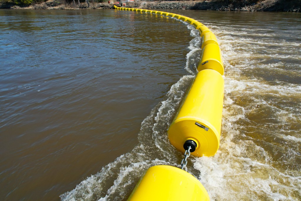 An ODINFloat public safety barrier with 30-inch diameter floats installed in the tailrace of a large hydropower plant, preventing unauthorized downstream access to dangerous water currents.