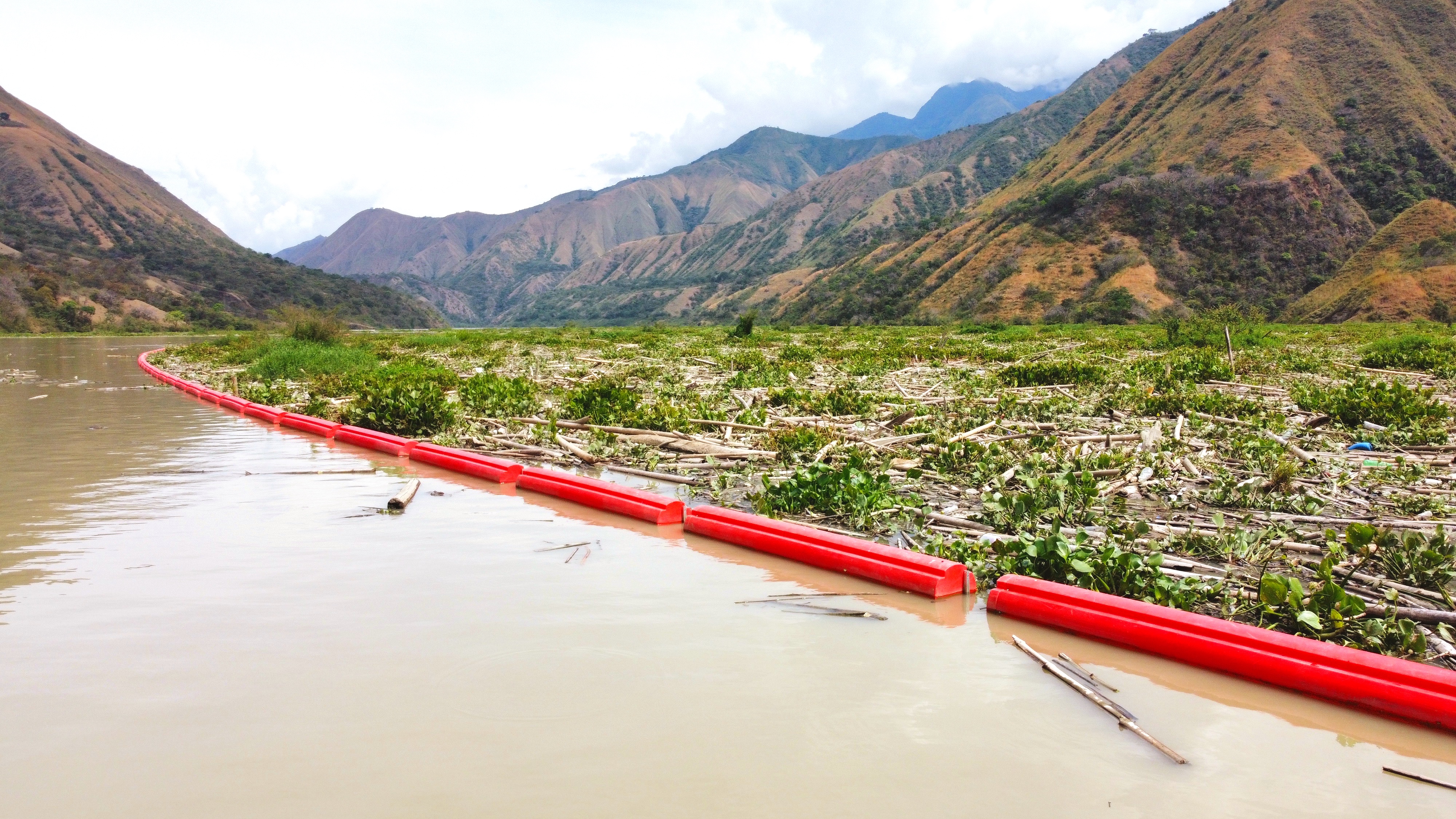 A floating debris barrier installed in a river to control logs, vegetation, and plastic waste. The barrier helps prevent debris from obstructing hydropower intakes and improves water quality for energy production.